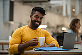 Afroamerikanischer Mann trinkt eine Tasse Kaffee und arbeitet an einem Laptop