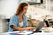 Erwachsene weibliche Grafikdesignerin, die am Schreibtisch sitzend einen Laptop benutzt