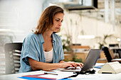 Adult female graphic deisgner using laptop while sitting at desk