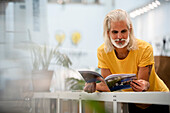 Männlicher erwachsener Designer, der sich beim Lesen einer Zeitschrift auf einen Tisch stützt