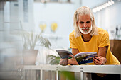 Adult male designer leaning on table while reading magazine