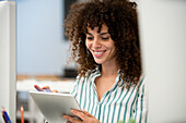 Junge erwachsene Geschäftsfrau, die ein digitales Tablet benutzt, während sie im Büro sitzt