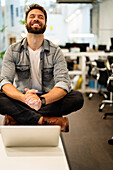 Männlicher Unternehmer, der einen Videoanruf am Laptop führt, während er auf dem Tisch sitzt