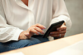 Mittelaufnahme einer Frau, die im Büro sitzend ein Smartphone benutzt