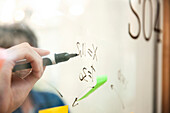 Close up of businessman writing on glass wall with black marker