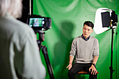Junger erwachsener Mann gibt ein Interview, während er vor einem Greenscreen sitzt