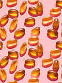 Composition of orange-coloured vitamin pills on a pink background in a bright studio viewed from above