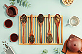 Beautiful set for traditional tea ceremony and tea collection in wooden spoons on light blue background flat lay
