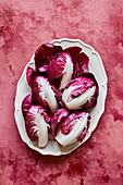 Raddichio-Blätter auf ovalem weißen Teller auf rosa Hintergrund