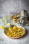 Chicken, lemon slices and capers in a copper pan with a napkin on the handle, bread and white wine