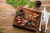 Gegrilltes Hirschsteak mit gebackenem Gemüse, Beerensauce und Rotwein auf Holzuntergrund