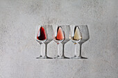 Red, rosé and white wine in glasses on a grey stone background. Wine bar, winery, wine tasting concept. Minimalistic trendy photography