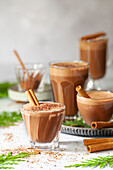 Heatproof glasses holding hot chocolate topped with grated chocolate and cinnamon sticks.