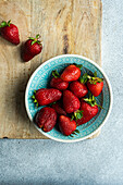 Ripe organic strawberries in a ceramic bowl on a concrete background