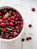Fresh ripe cherries in white stainless steel colander. Top view of wet red cherry over white woden background. Shallow DOF. Cherries aestetic. Copy space. Vertical.