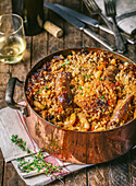 Klassisches französisches Cassoulet mit Huhn und Wurst in antikem Kupfertopf mit Weinglas und Flasche