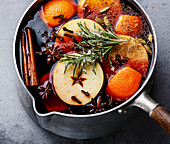 Mulled wine hot drink with citrus, apple and spices in aluminum casserole and rosemary sugar close-up