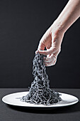 Squid pasta on a white plate with women's hands