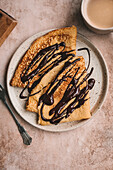 Crêpes drizzled with melted dark chocolate on a ceramic plate