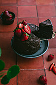 Schokoladenkuchen mit frischen Erdbeeren vor einem Terrakotta-Hintergrund