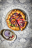Rustic Plum Galette, sliced, with red wine caramel sauce and a fresh rosemary sprig on intricate lace background