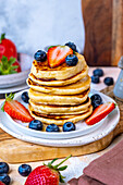 A stack of pancakes garnished with blueberries and strawberries on a white plate.