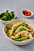 Vegetable gyoza noodles with sugar snaps, coriander and chilli on a grey surface
