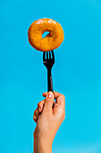 Anonymous person showing plastic fork with delicious sweet doughnut in front of light blue background in studio