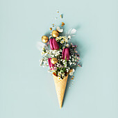 Easter composition. Ice cream cone with beautiful flowers and golden easter eggs on blue background flat lay