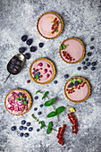 Arrangement aus vier kleinen Törtchen, gefüllt mit Beerencreme, dekoriert mit frischem Obst und Minze