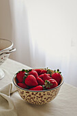 Bowl of strawberries on a table next to a window