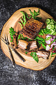 Sliced crispy pork belly on a wooden plate with forks, sliced gherkins and radishes