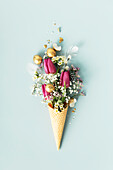 Easter composition. Ice cream cone with beautiful flowers and golden easter eggs on blue background flat lay