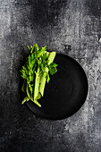 Top view of celery sticks on black plate on concrete dark surface