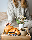 Breakfast in bed with freshly baked croissants with blueberry jam and tea in a mug.