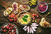 Pate spread in glass jar on wood board with roasted grapes, radishes, pickles and baguette