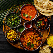 Indian food curry butter chicken, palak paneer, chiken tikka, biryani, vegetable curry, papad, dal, palak sabji, jira alu, rice with saffron on a dark background