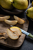 A halved pear, slices and a knife lie on a chopping board. Fruit on a plate