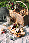 Picknickszene mit einem Korb, Kaffee und einer Tafel mit Weintrauben, Käse und einem Baguette