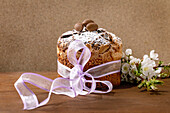 Homemade Italian traditional Easter panettone cake decorated with chocolate eggs, pink ribbon and blooming cherry blossoms standing on wooden table. Traditional European Easter cake. Place to copy