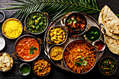 Indisches Essen Curry-Butterhähnchen, Palak Paneer, Chiken Tikka, Biryani, Gemüsecurry, Papad, Dal, Palak Sabji, Jira Alu, Reis mit Safran auf dunklem Hintergrund