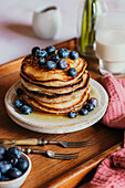 Stack of pancakes with blueberries, syrup and a glass of milk