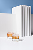 Front view of transparent glasses filled with cold, refreshing Scotch whiskey with ice cubes on a white surface against a white and blue background