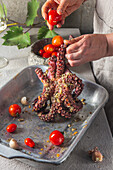 Frau hält rohen Oktopus und schmiert ihn mit Gewürzen und Tomaten ein