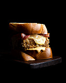 Appetitlicher Burger mit frischen Brötchen und Käse auf Holzbrett serviert auf schwarzem Hintergrund