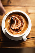 Person stirring coffee in a white cup on a wooden table