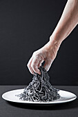 Squid pasta on a white plate with women's hands