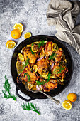 Chicken thighs in cast iron skillet with fresh and roasted lemons, fennel and shallots on gray background