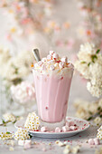 A pink hot chocolate drink served over ice and topped with whipped cream and marshmallows.