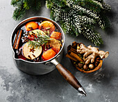 Mulled wine hot drink with citrus fruits, apples and spices in aluminium casserole and fir branch on concrete background